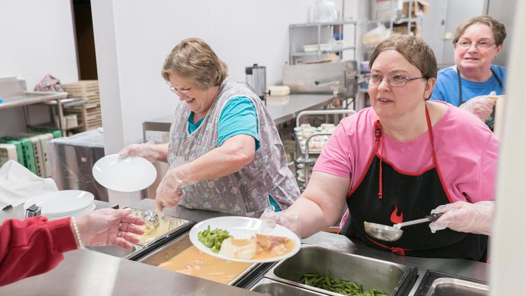 several workers in a cafeteria setting serving plates of food