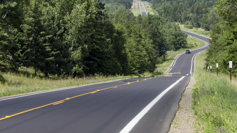 a newly paved asphalt road winding through a scenic wooded area