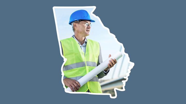 An architect in a safety vest and hard hat holding rolled construction plans at a building site